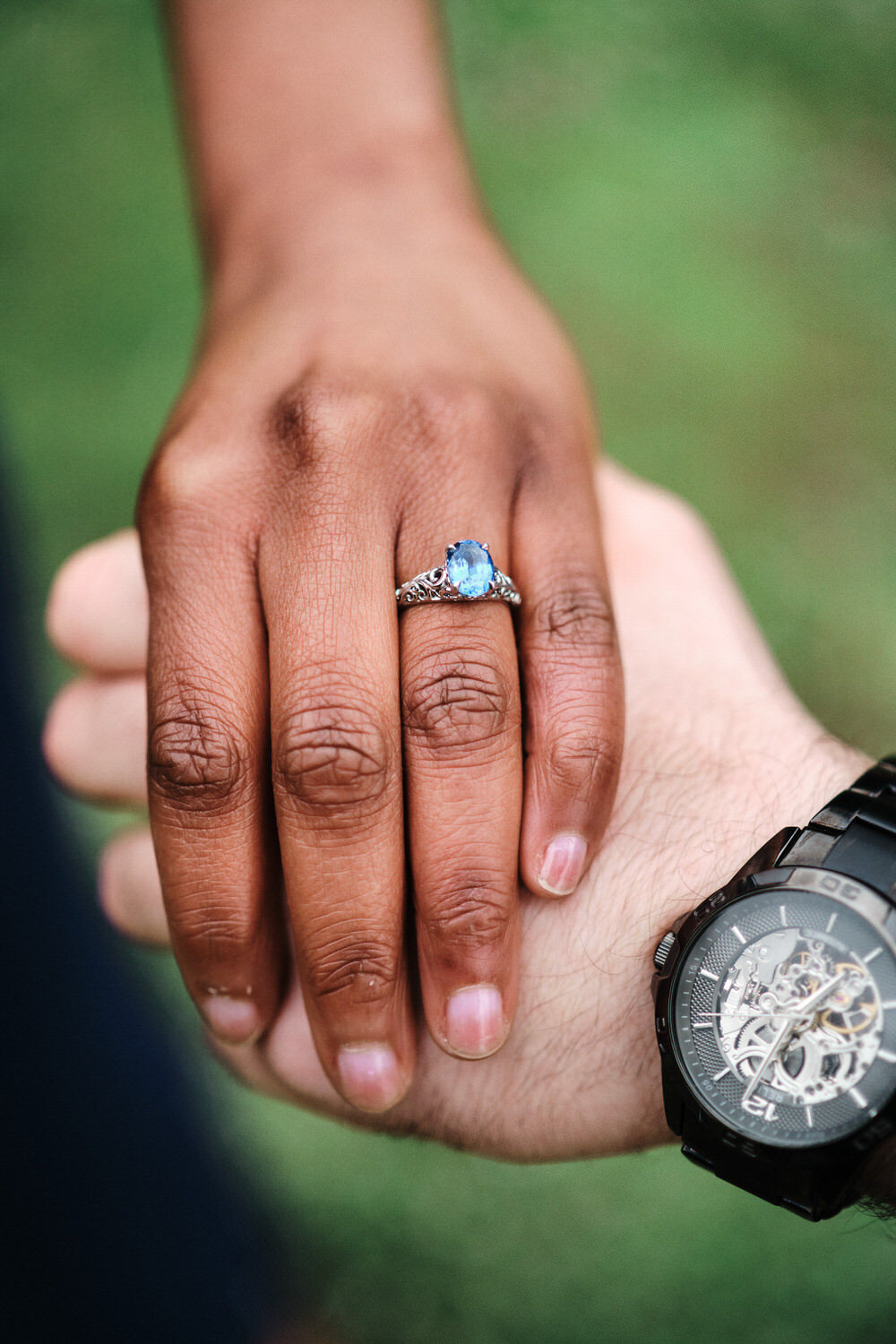 Close up of a couple holding hands with the engagement ring prominent