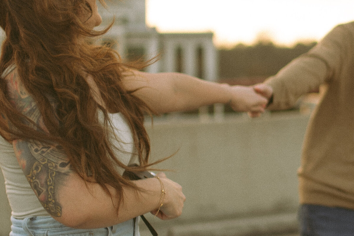a couple holding hands outside holding a vintage film camera and wind blowing in the womans hair.