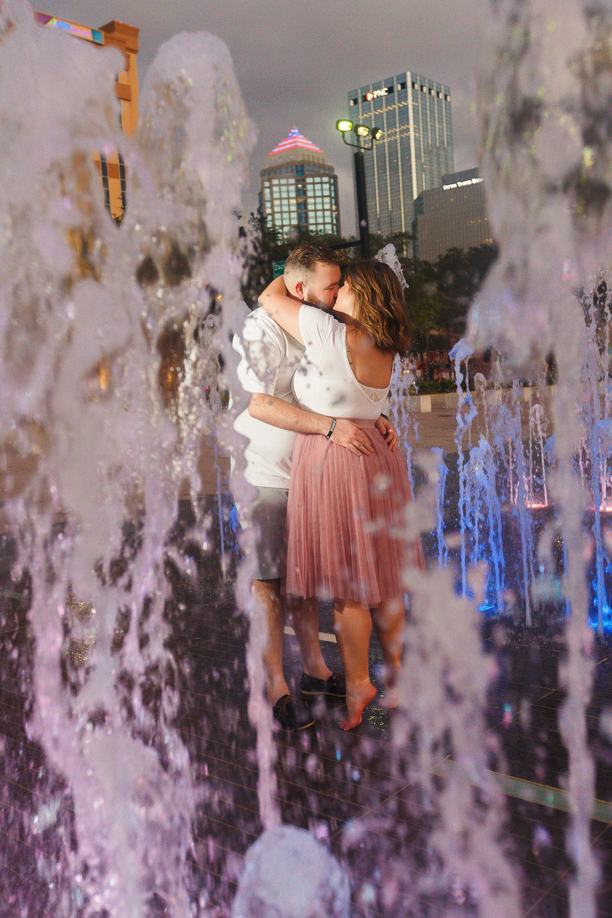 engaged couple in passion kissing embrace in the fountain spray at Curtis Hicks Park in Tampa Florida
