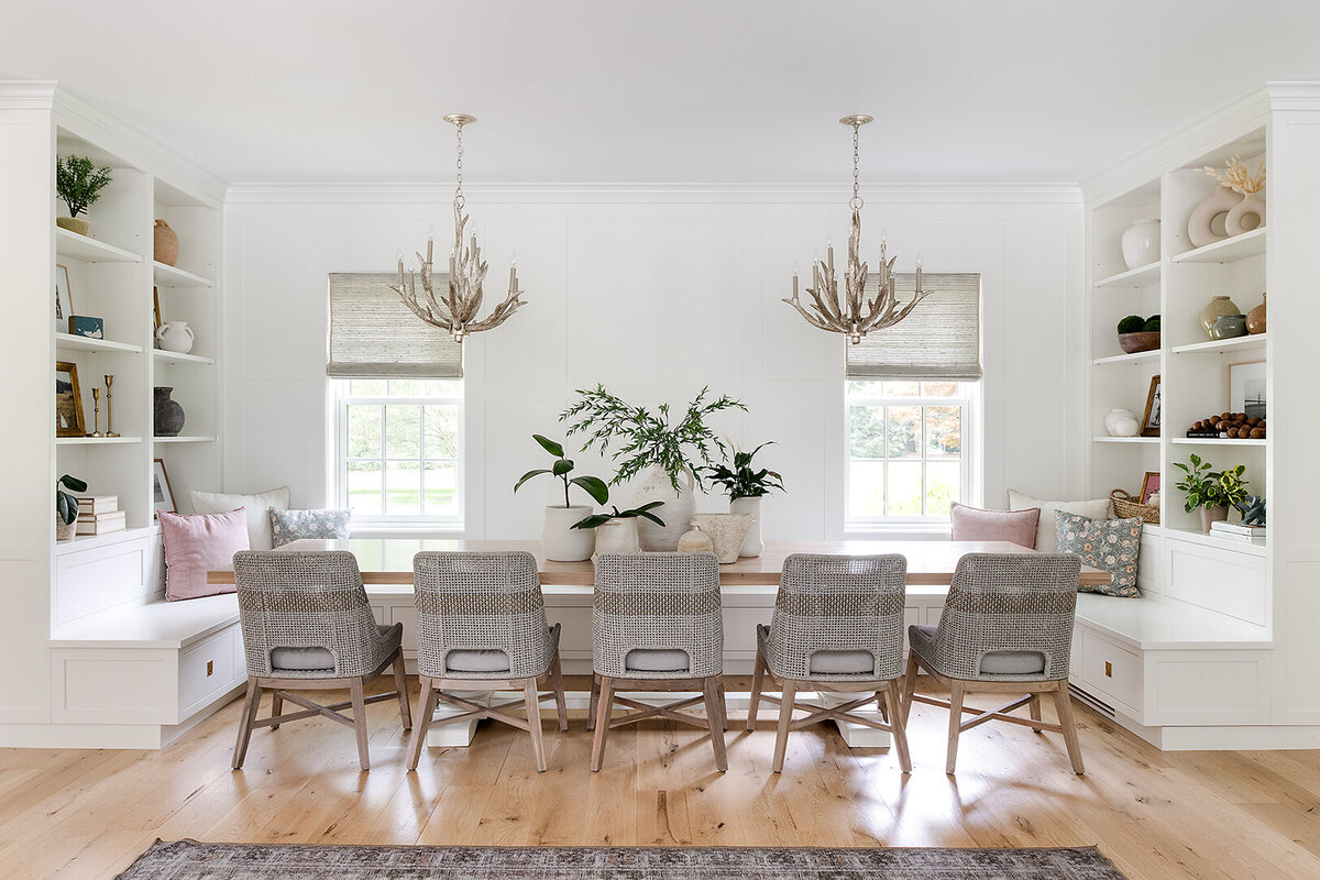 white dining room with long table, two chandeliers and bench seating