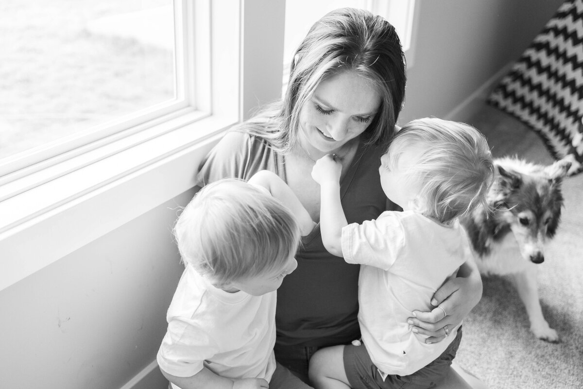 Mother sitting by the window with her two young children and dog, sharing a quiet, intimate moment at home.