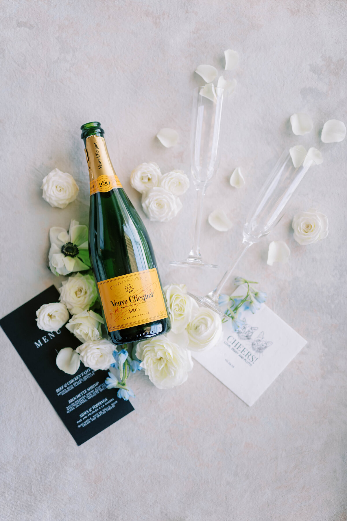 Flat lay of wedding invitation suite, white flowers, and champagne bottle
