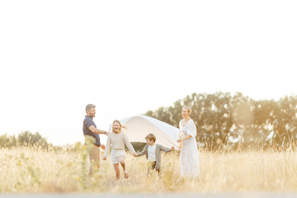 A family standing in a grassy field at a Fort Worth TX park as they play with their children for family photos.