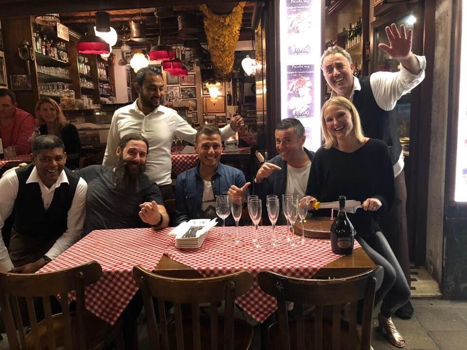 A group of friends celebrate a birthday with cake and champagne at a traditional Venetian restaurant and wine bar, Ai Specchieri near St. Mark's Square 
