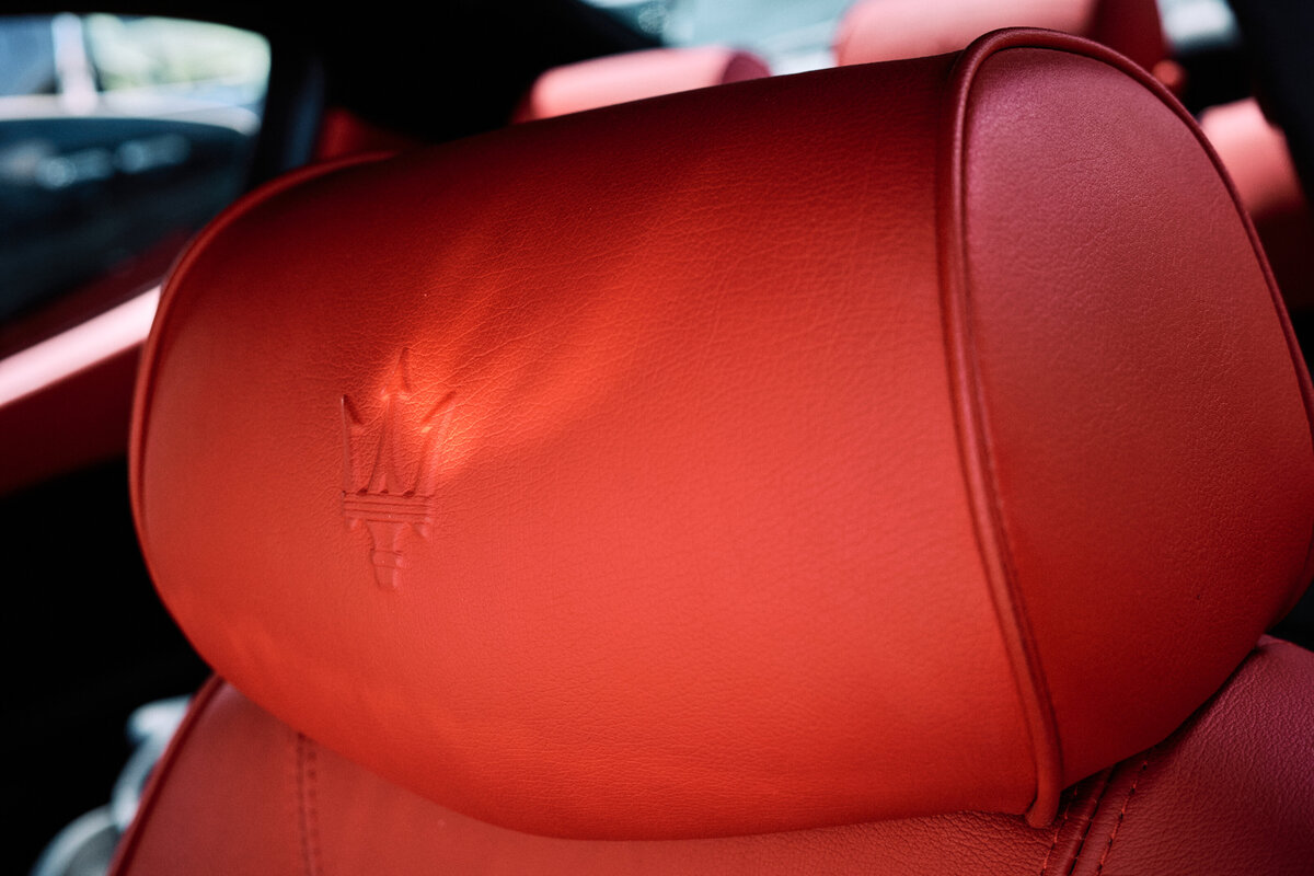 Detail shot of a Maserati headrest upholstered in rich red leather with the iconic trident logo embossed for a luxurious, sporty feel.