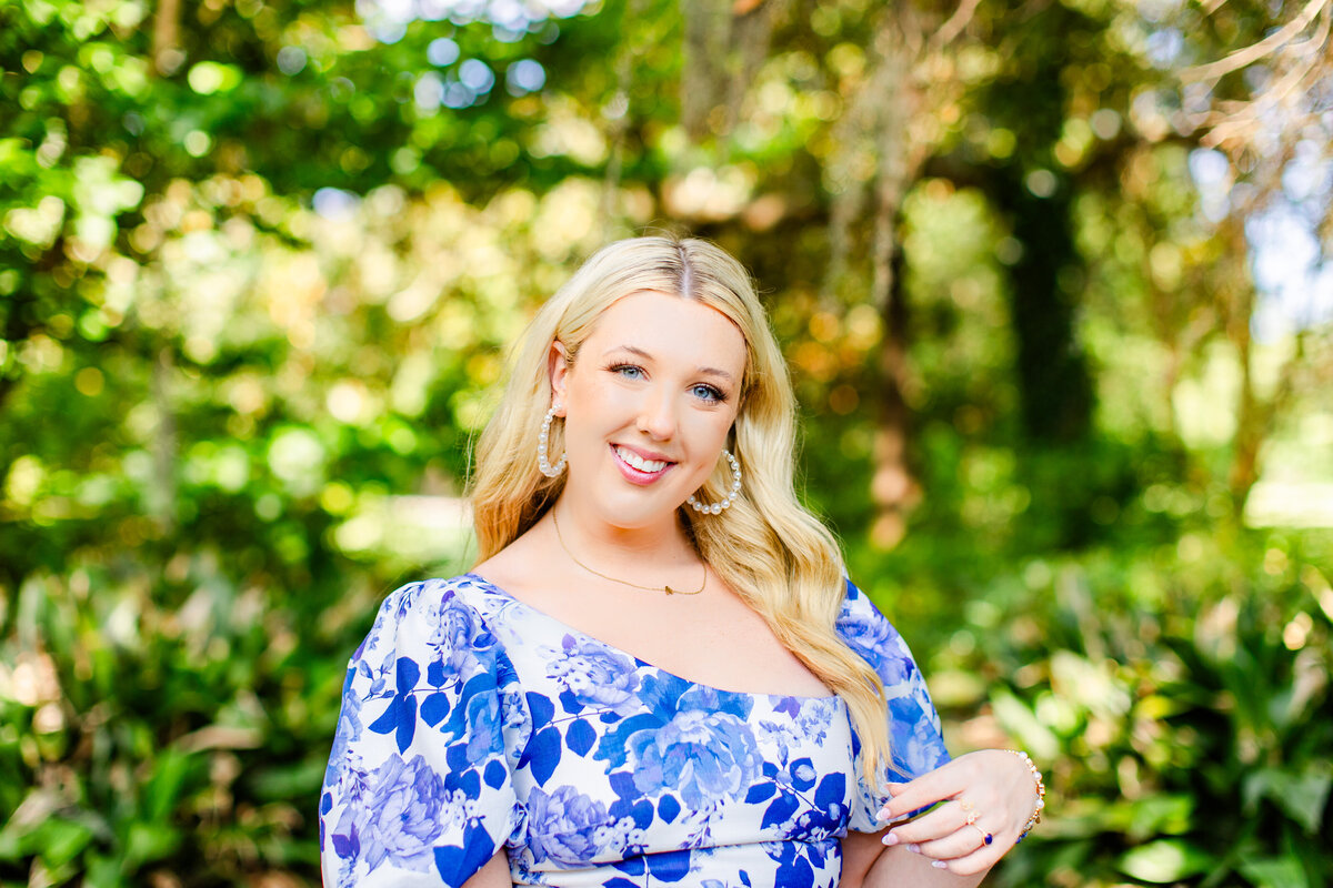 high school senior with blue and white dress posing in front of lush green bushes
