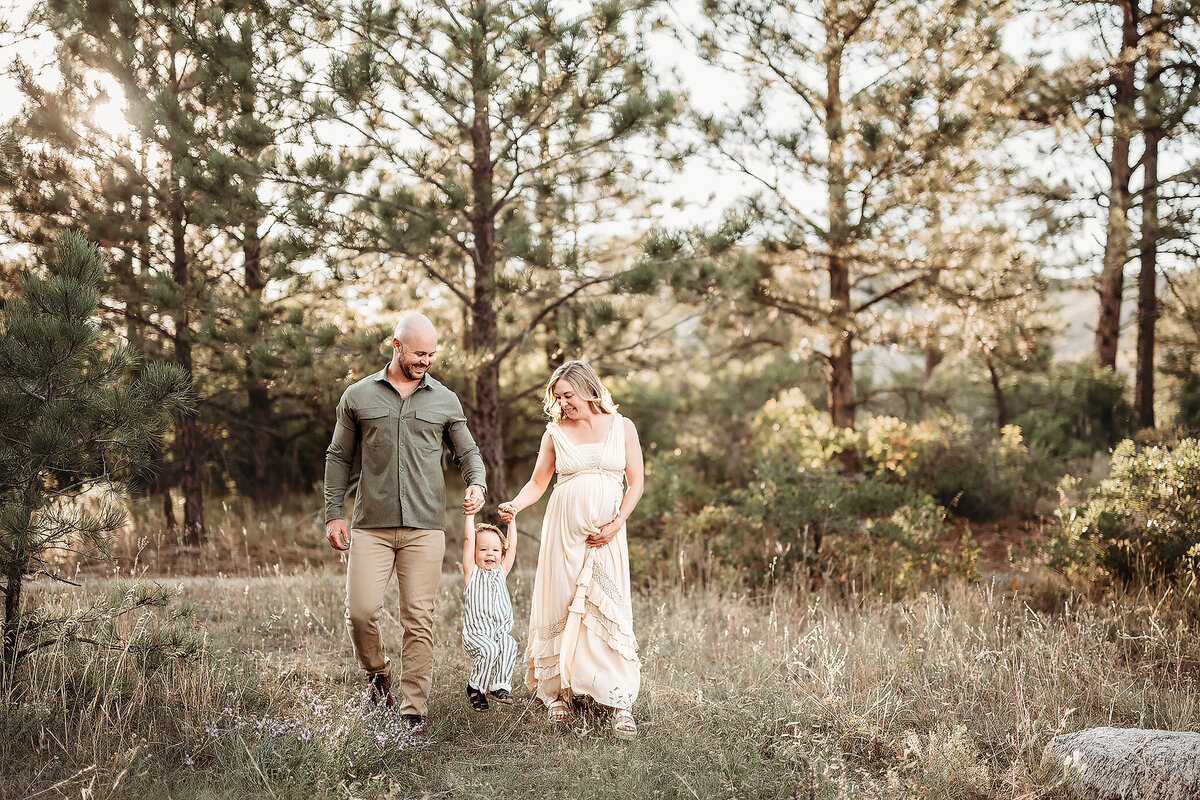 family of three holding hands walking through forest