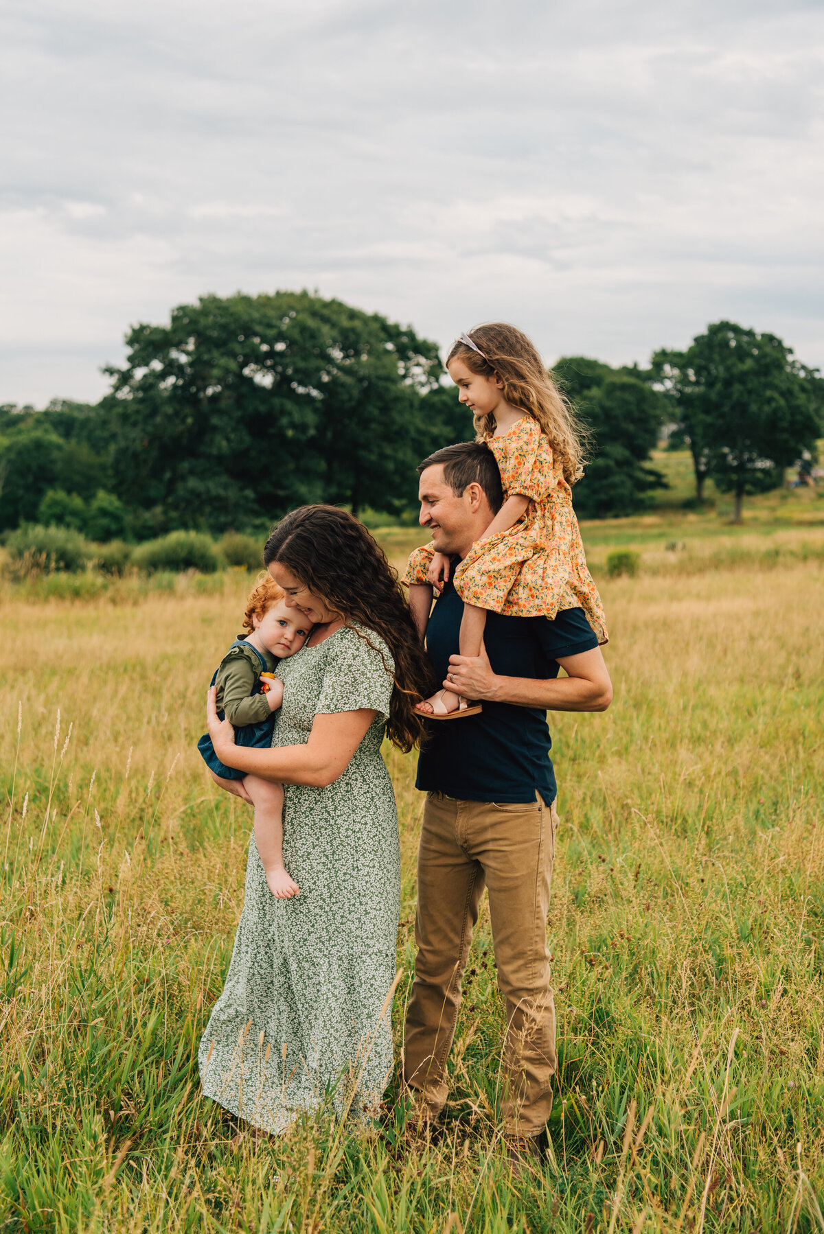 Family of four, embracing in field at sunset