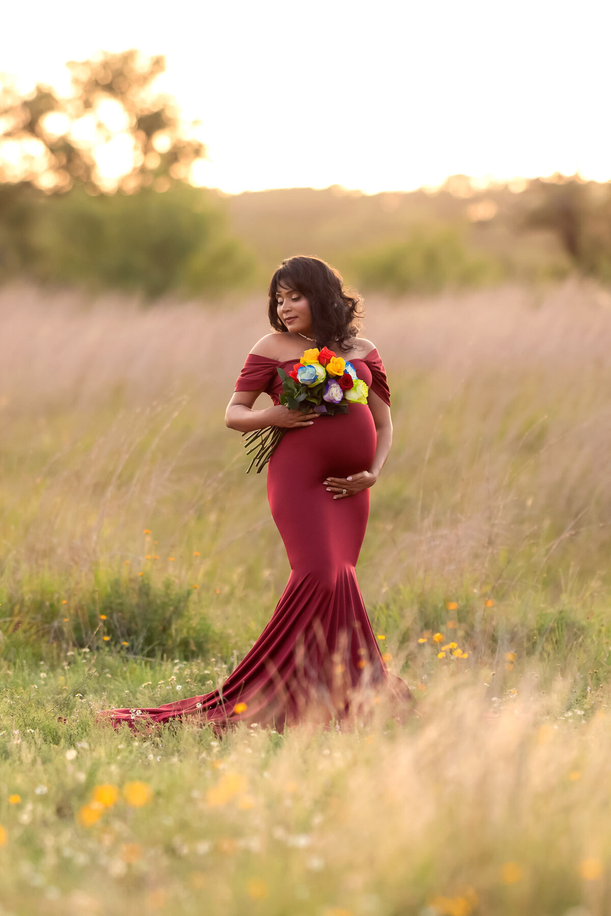 Outdoor maternity photography featuring pregnant woman in flowing red gown in natural meadow setting