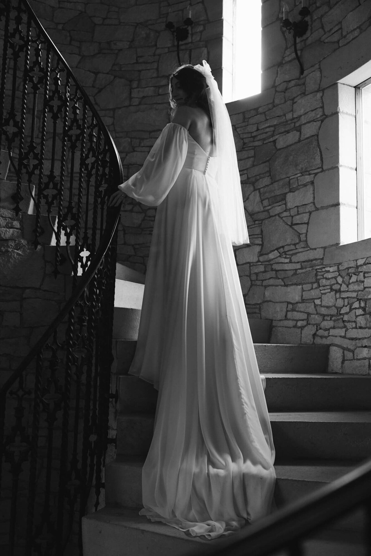 A bride stands in a round stairwell with her dress train draping down the stairs.