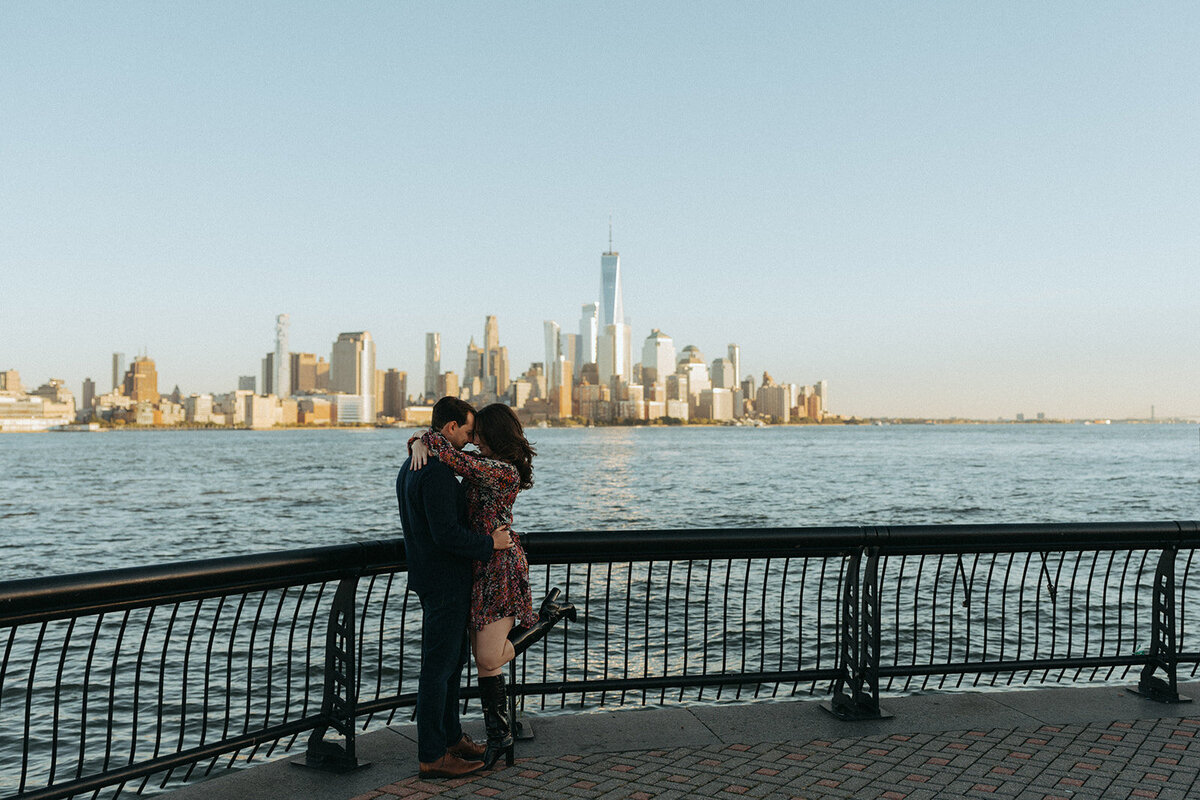 couple kissing with city skyline in the background during NYC engagement photos, captured by Elsie Goodman, an NYC engagement and couples photographer