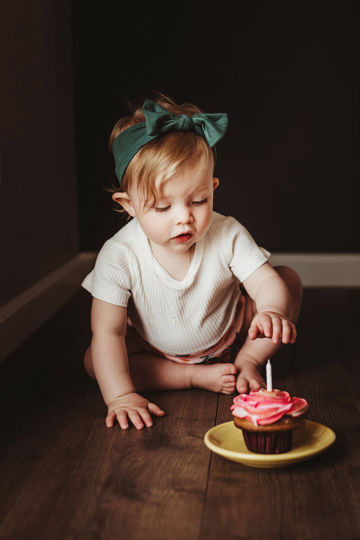 A little girl with a green hairband is about to dig into a cupcake with pink icing.