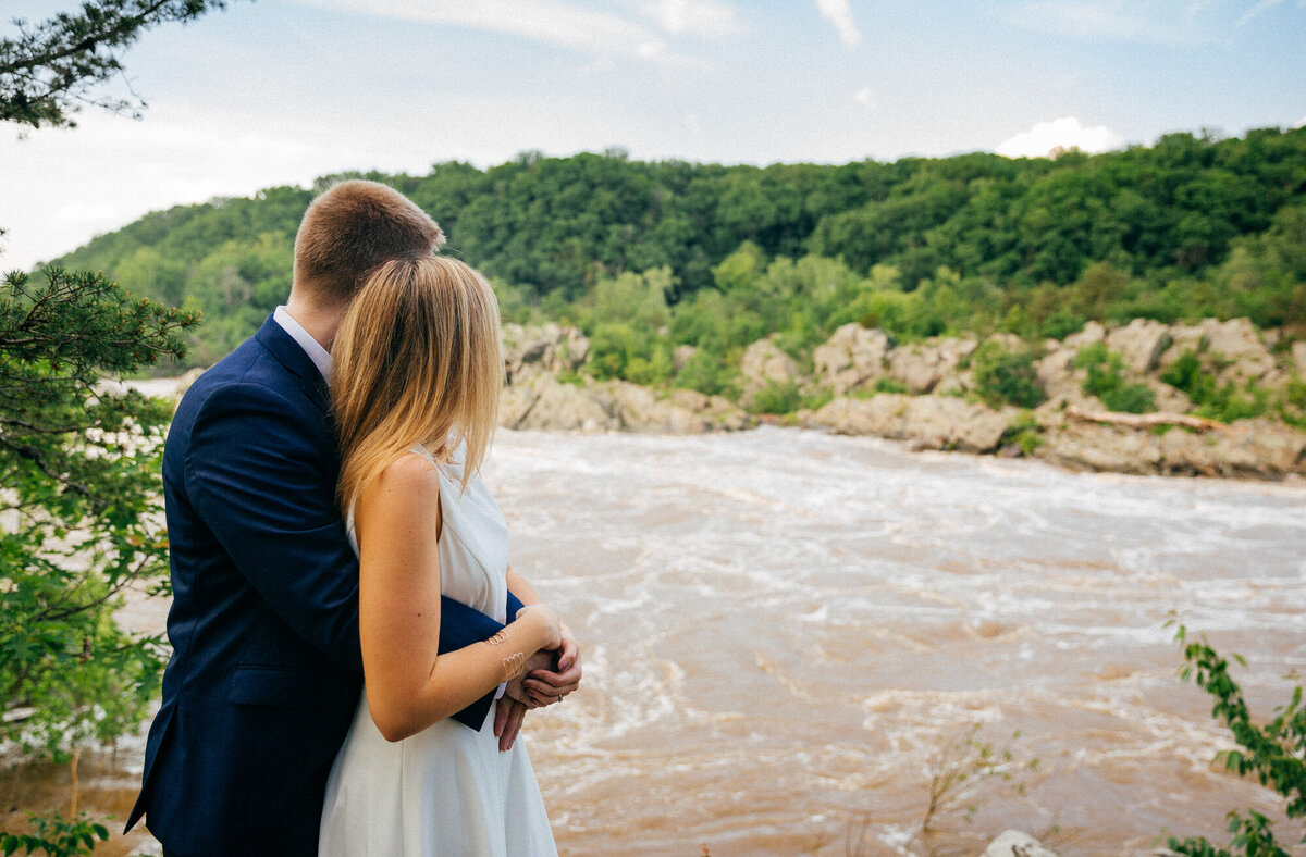 Engaged couple hugging and looking out to the water at Great Falls Virginia