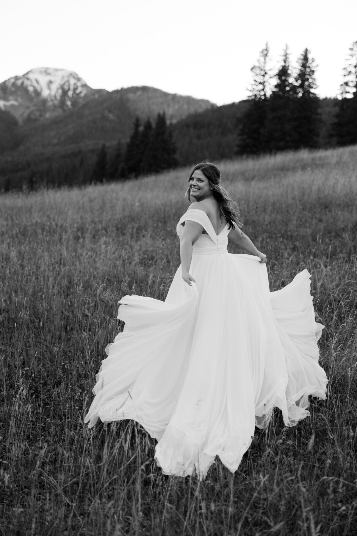 Black and white photo of bride twirling and smiling in an open field.
