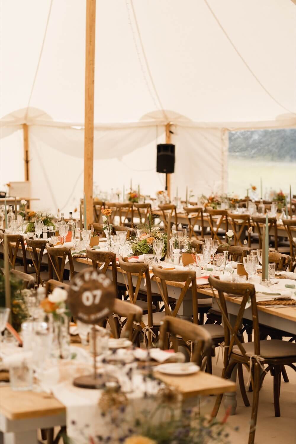 A beautiful rustic wedding breakfast set up with long tables inside of a pole marquee