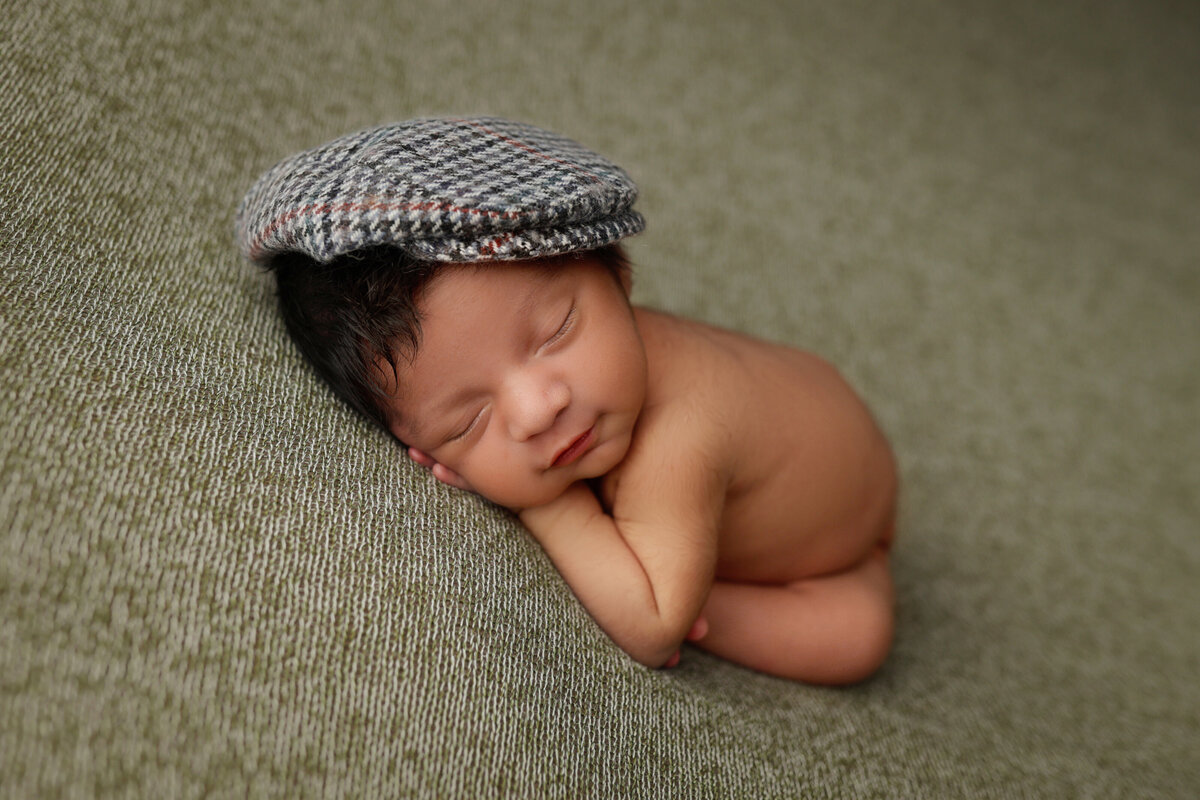 baby boy sleeping on a green blanket wearing a hat