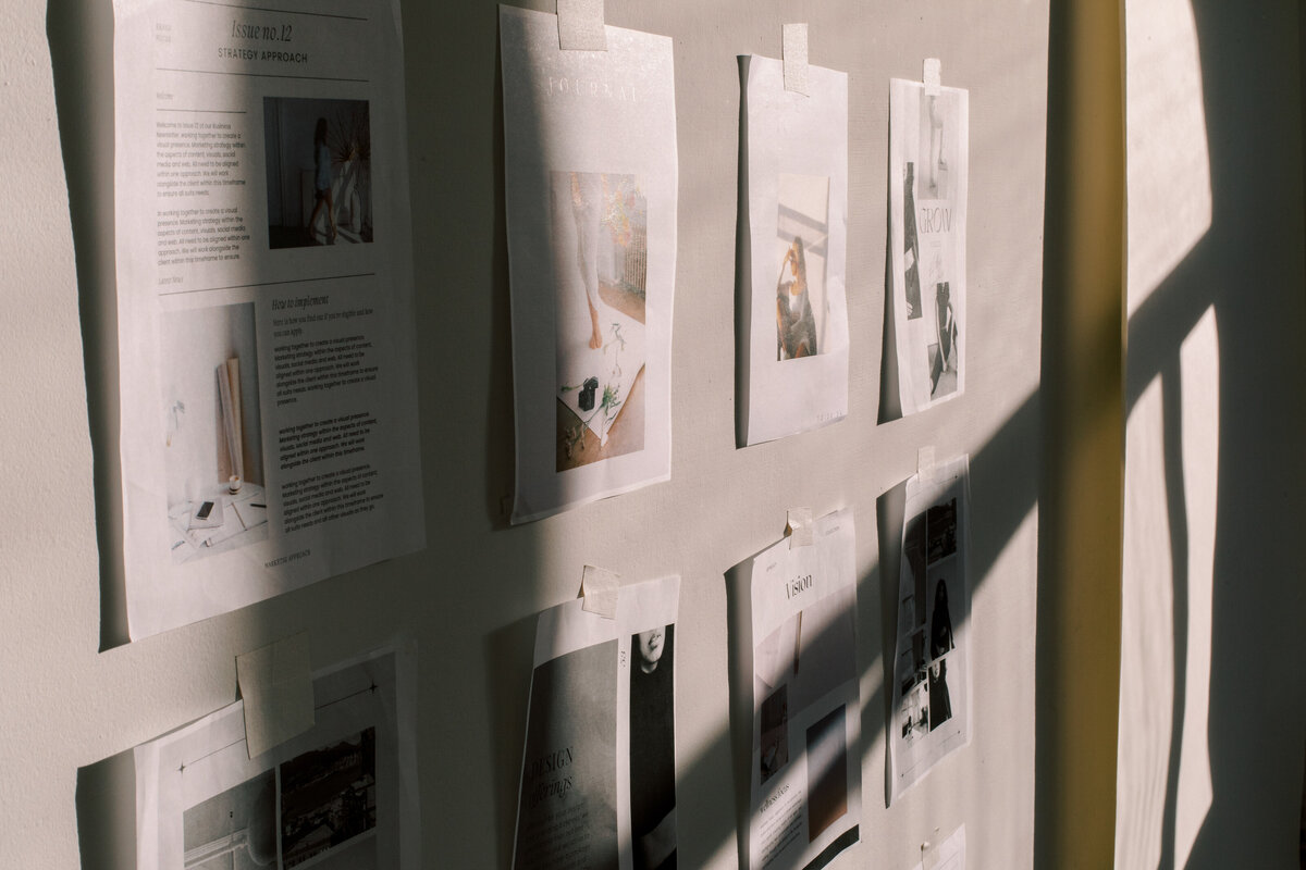 Photos and printed articles are taped to a sunlit wall, casting shadows, reminiscent of branding and website design for female entrepreneurs.