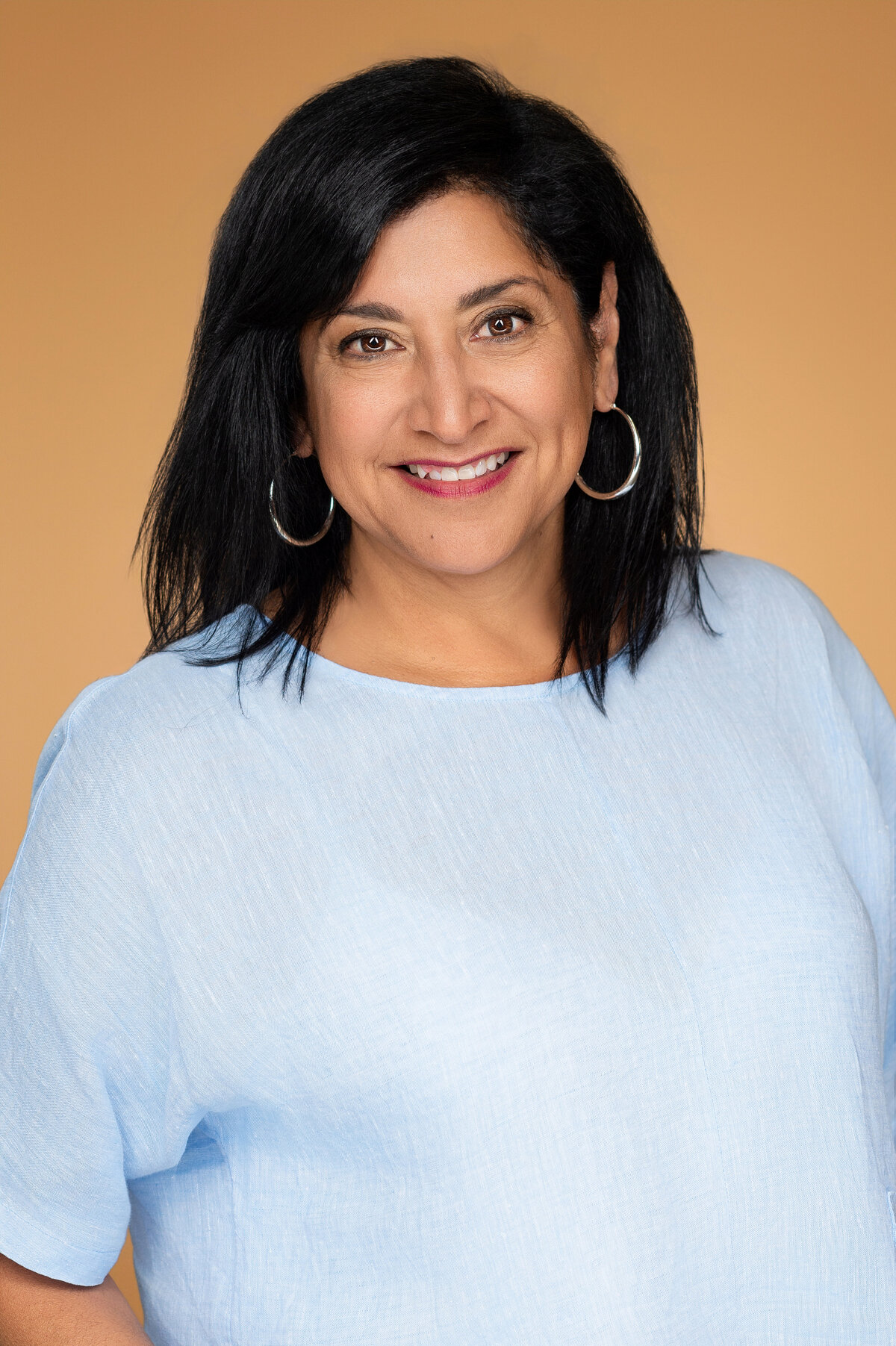 Professional headshot of a smiling woman against a solid caramel backdrop
