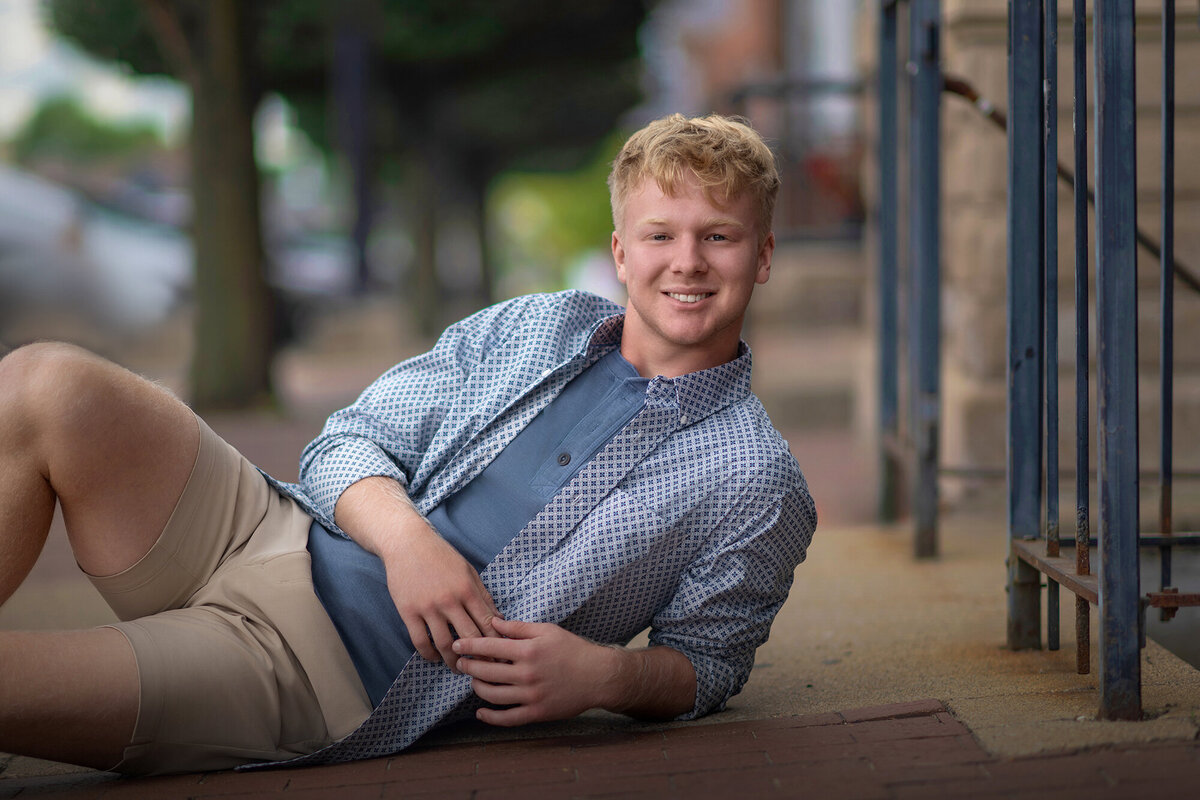 A high school grad lays on the street in khakis and blue shirts