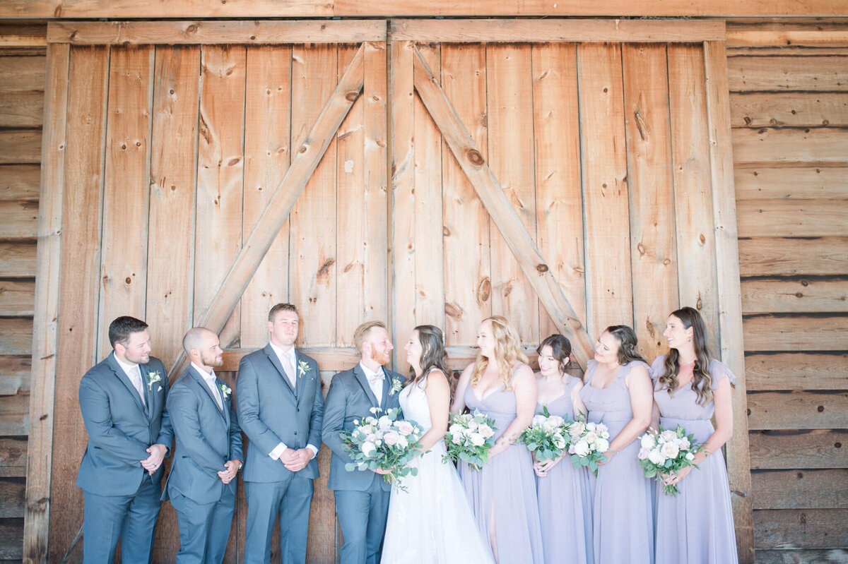 Wedding party lined up against barn doors  looking at bride and groom