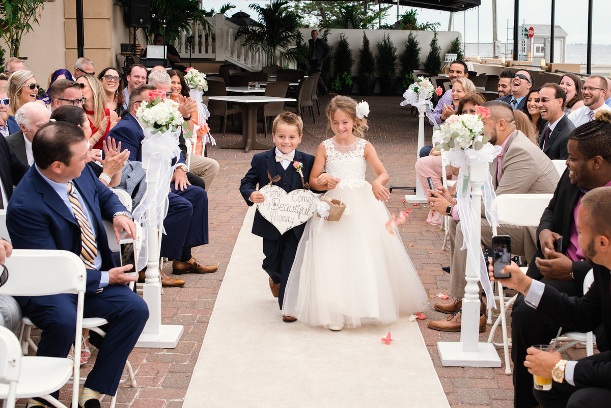 photo of ring bearer and flower girl walking down the aisle for outdoor wedding ceremony at Lombardi's on the Bay