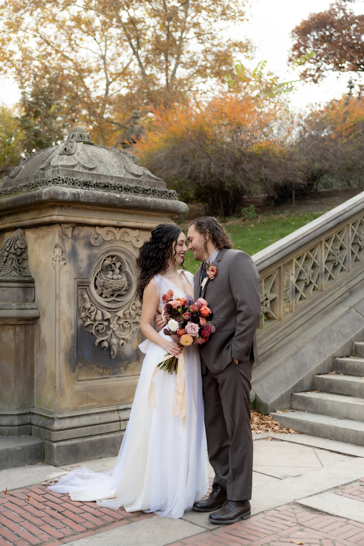 Bride and groom walking up historic stone steps in Central Park, NYC, surrounded by golden fall foliage during their intimate elopement.
