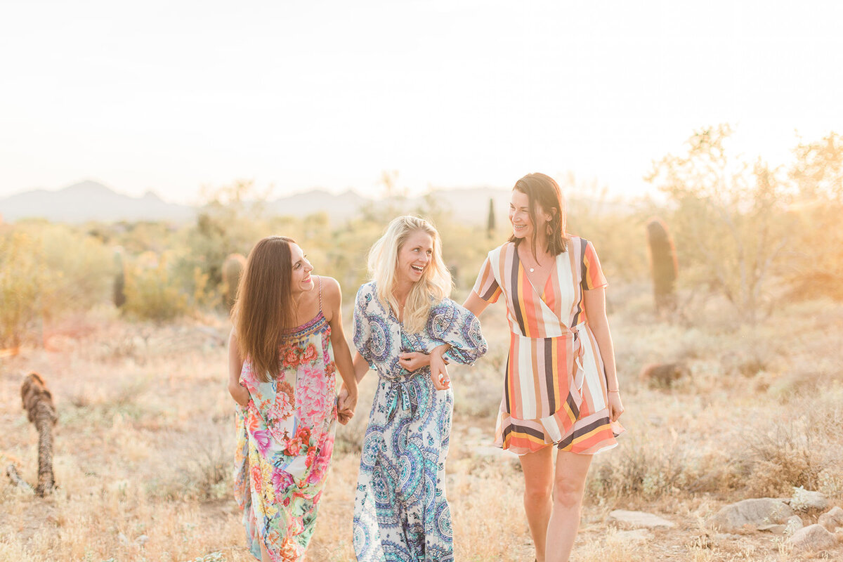 three women waling in flowly dresses while laughing at each other