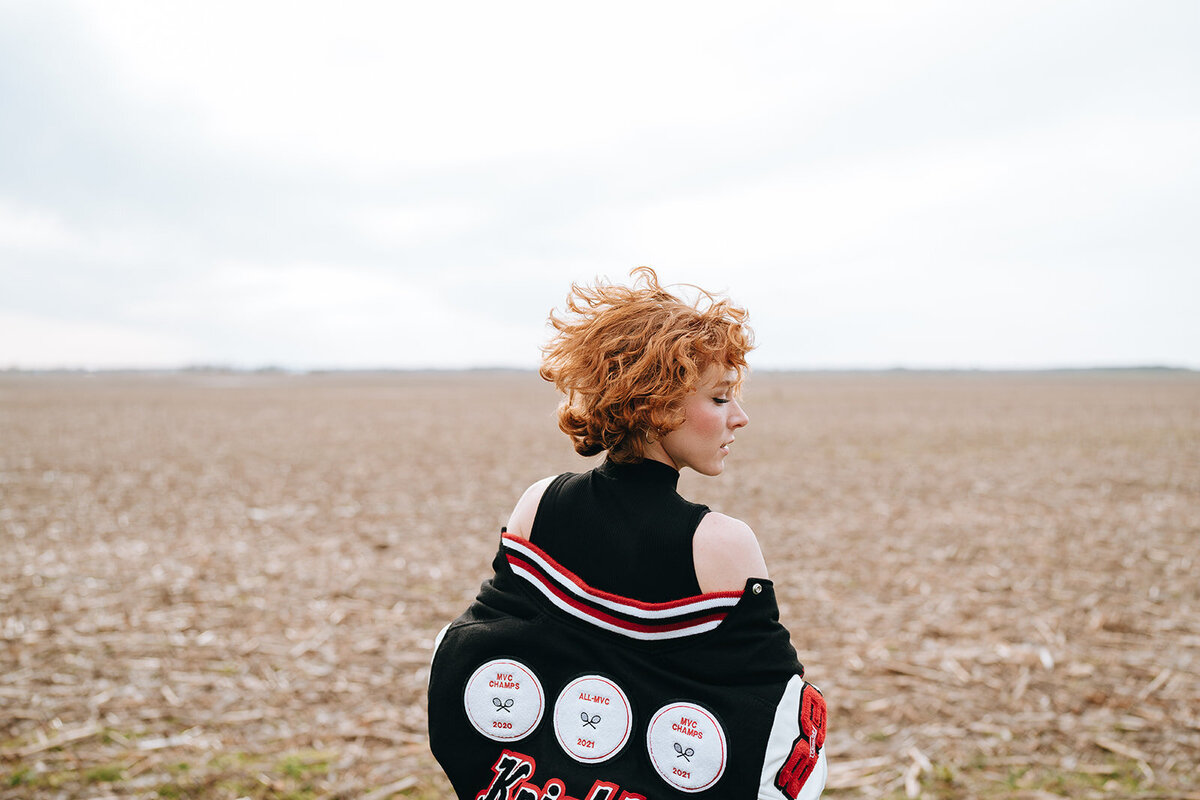 high school senior posing outside with letterman jacket