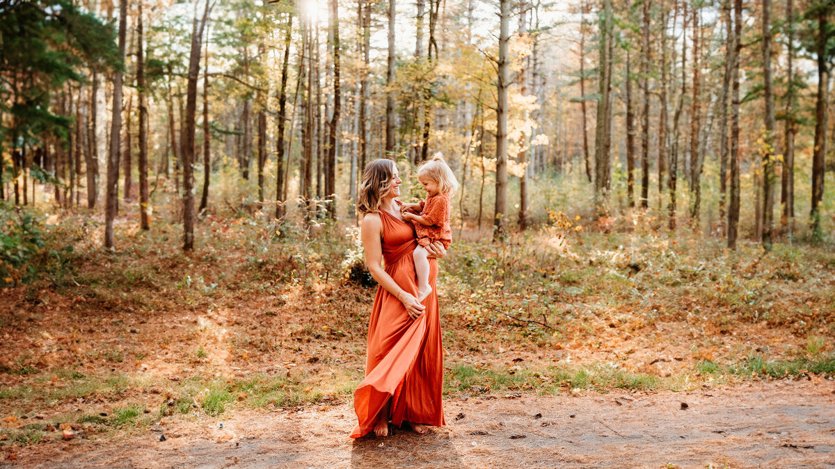 An expecting mom is cupping her baby bump, while holding her toddler daughter's hand. Photo taken by Philadelphia maternity photographer, Kristi