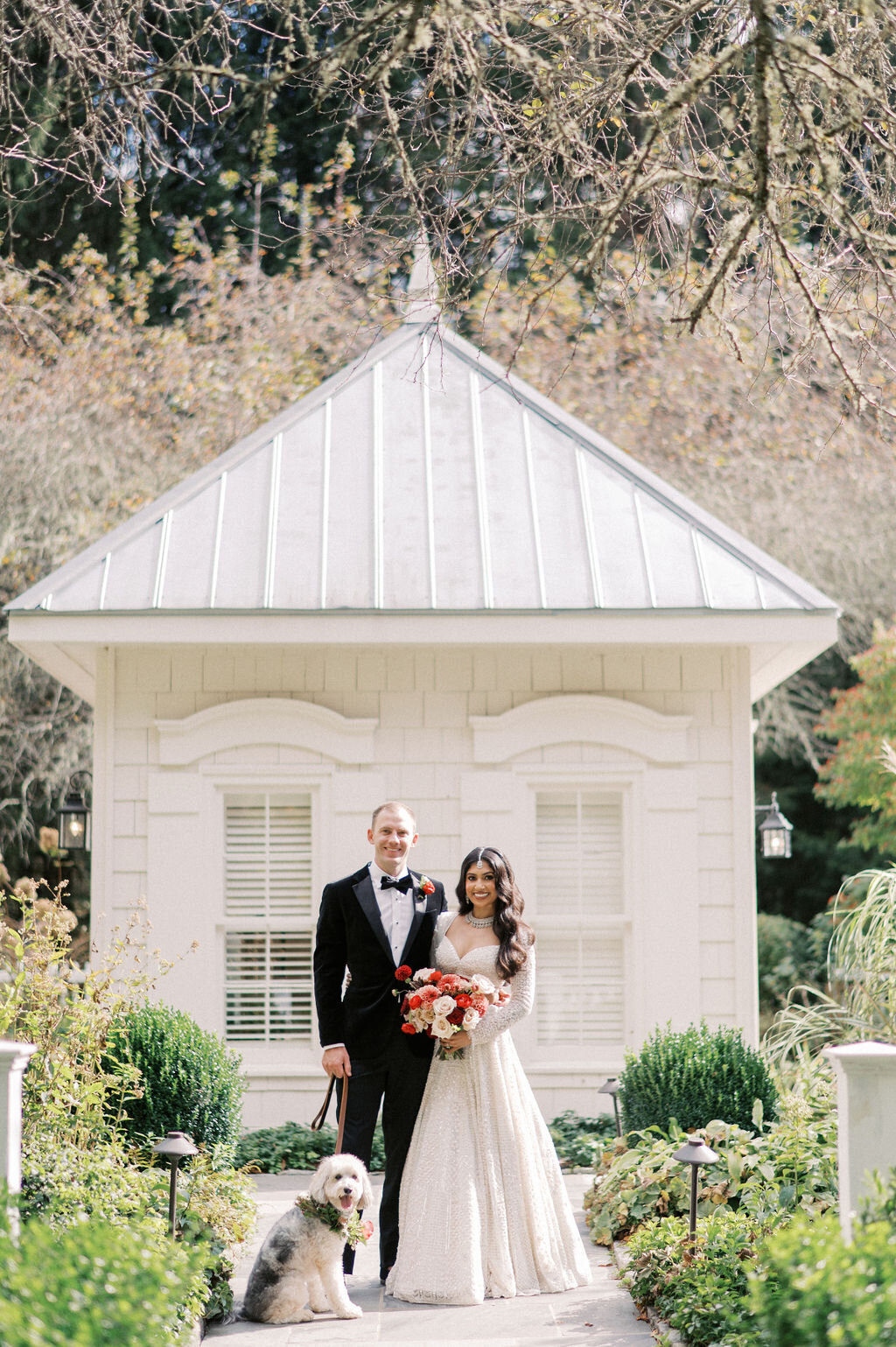 Bride and groom standing with their dog wearing a floral collar during wedding portraits at Old Edwards Inn in Highlands, North Carolina.