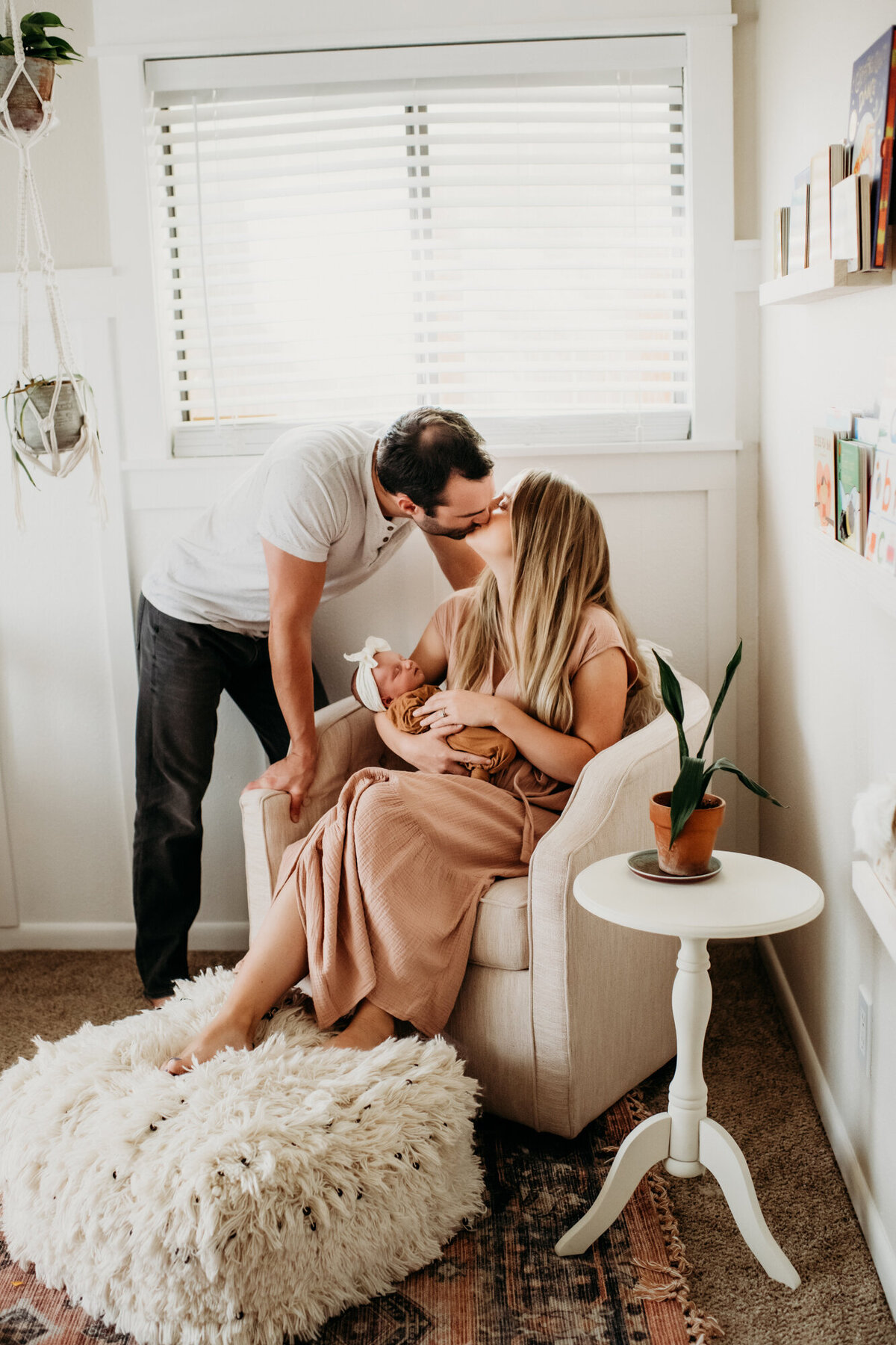 Newborn Photographer, Mom and dad kissing in the chair while holding their baby girl.