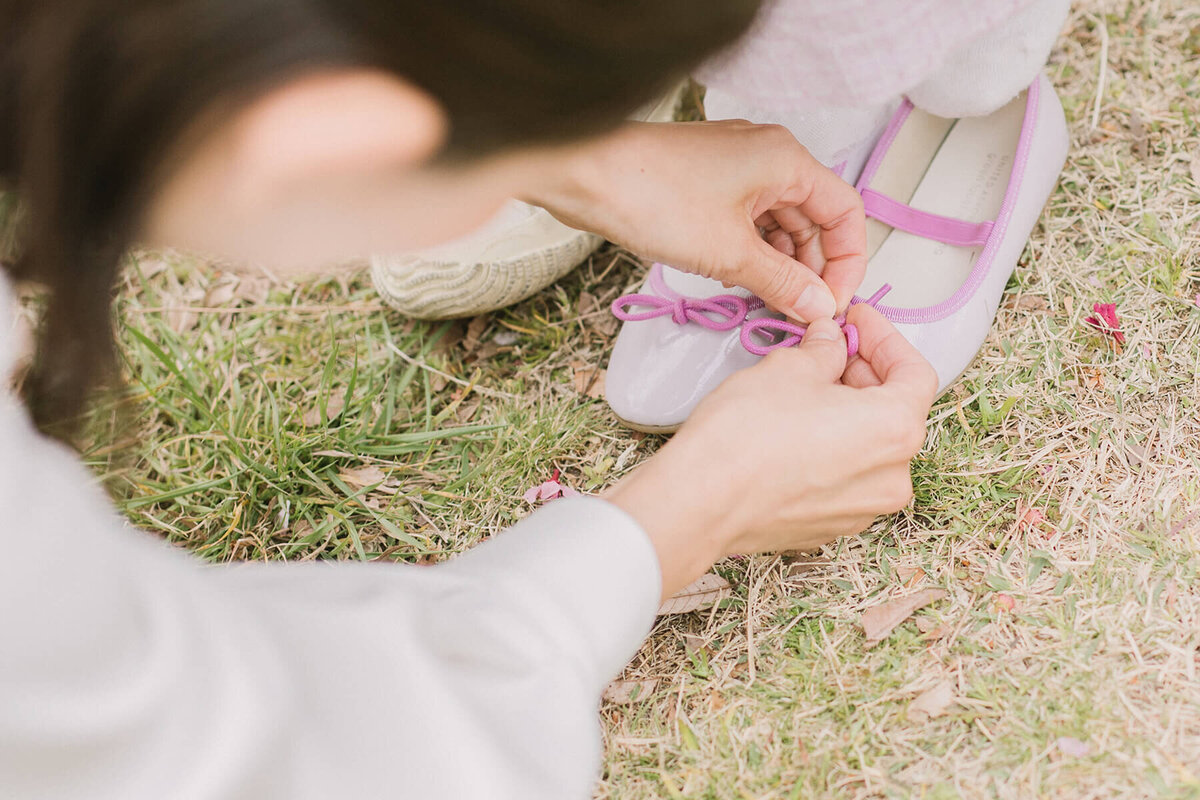 ママが女の子の紫色のパンプスの靴ひもを直しているショット。
