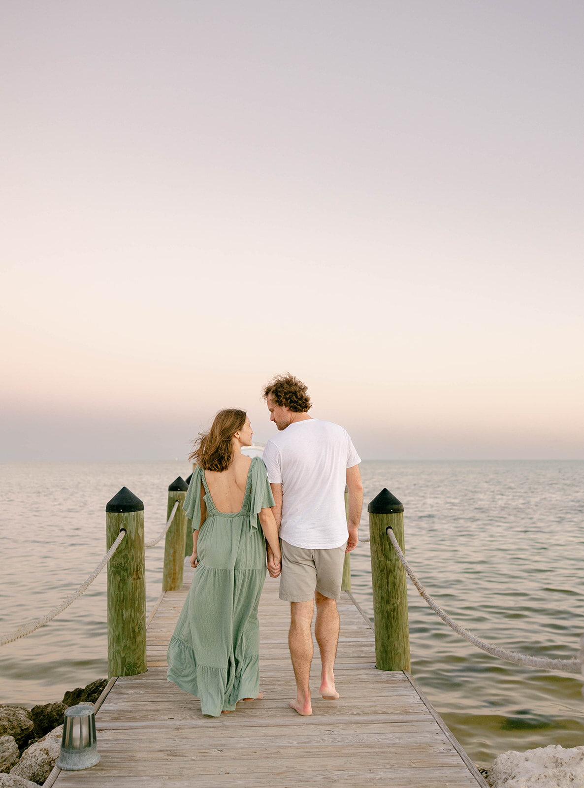 A family walks hand in hand on a wooden dock during a sunset beach session in the Florida Keys. Captured by Claudia Amalia, Florida Keys family photographer.