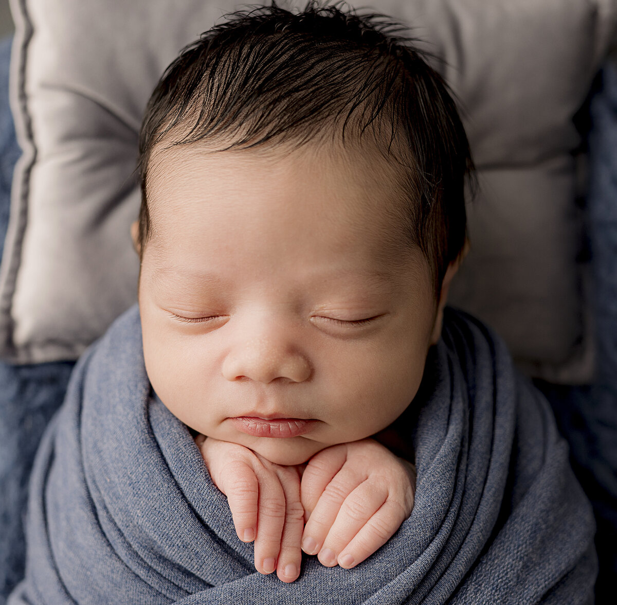 newborn baby face with hands grabbing on the wrap