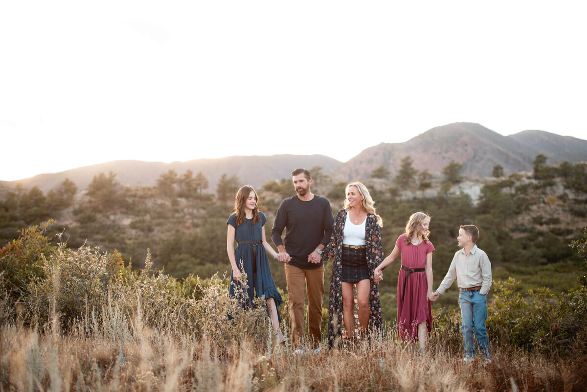 A family of 5 hold hands and laugh while exploring a mountain trail