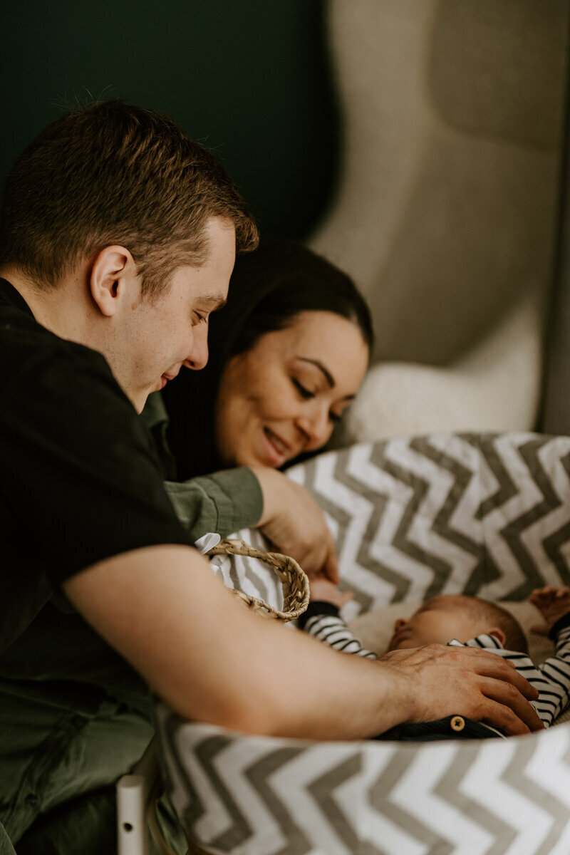 Parents faisant des papouilles à leur bébé endormi dans son panier, posant pour Laura, photographe professionnelle en vendée.