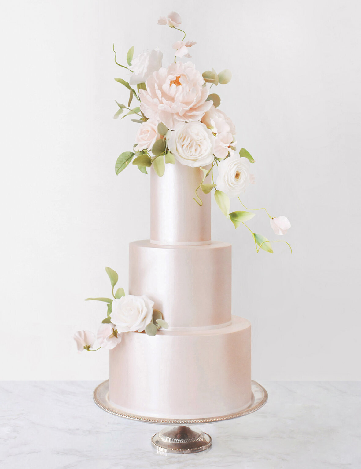 An elegant pale pink wedding cake with a shiny satin finish and pale pink sugar flowers on top