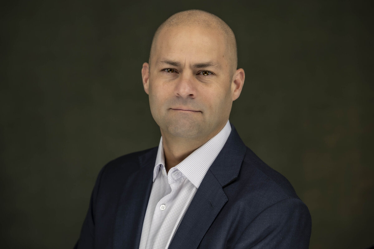 Business portrait of a bald man in a navy suit and light dress shirt, smiling confidently against a dark background, photographed by Rob Faber Photography in CT.