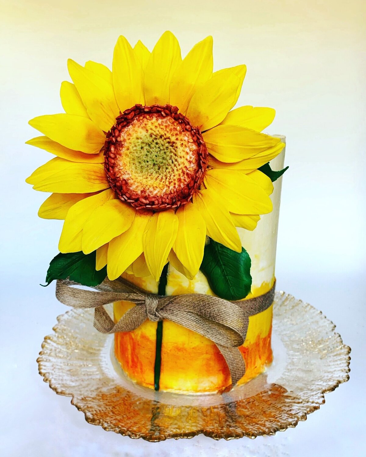 Lemon coconut cake filled with passion fruit curd. Hand-painted buttercream finish in shades of orange and yellow. Decorated with large single handcrafted gumpaste sunflower and burlap bow