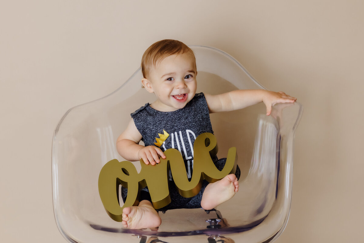 Cake Smash Photographer, a baby sits on chair and smiles