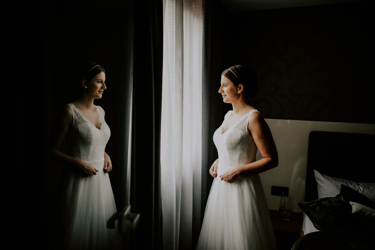 Braut im Brautkleid steht am Fenster beim Getting Ready der Braut im Hotel Rössle Stimpfach-Rechenberg mit Hochzeitsfotograf Ellwangen Anastasia Walther