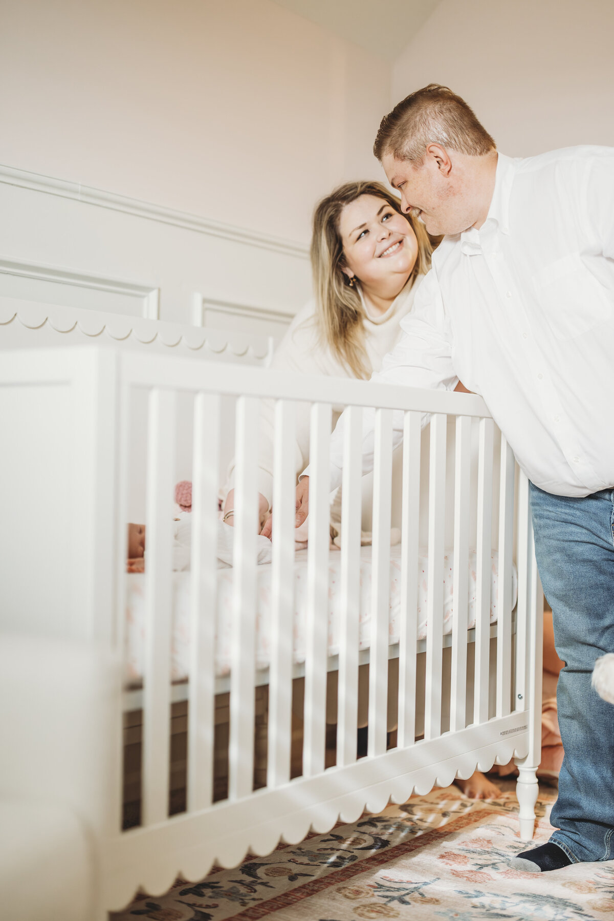 Parents peeking over the side of a white crib during a playful Kansas City family photography session.