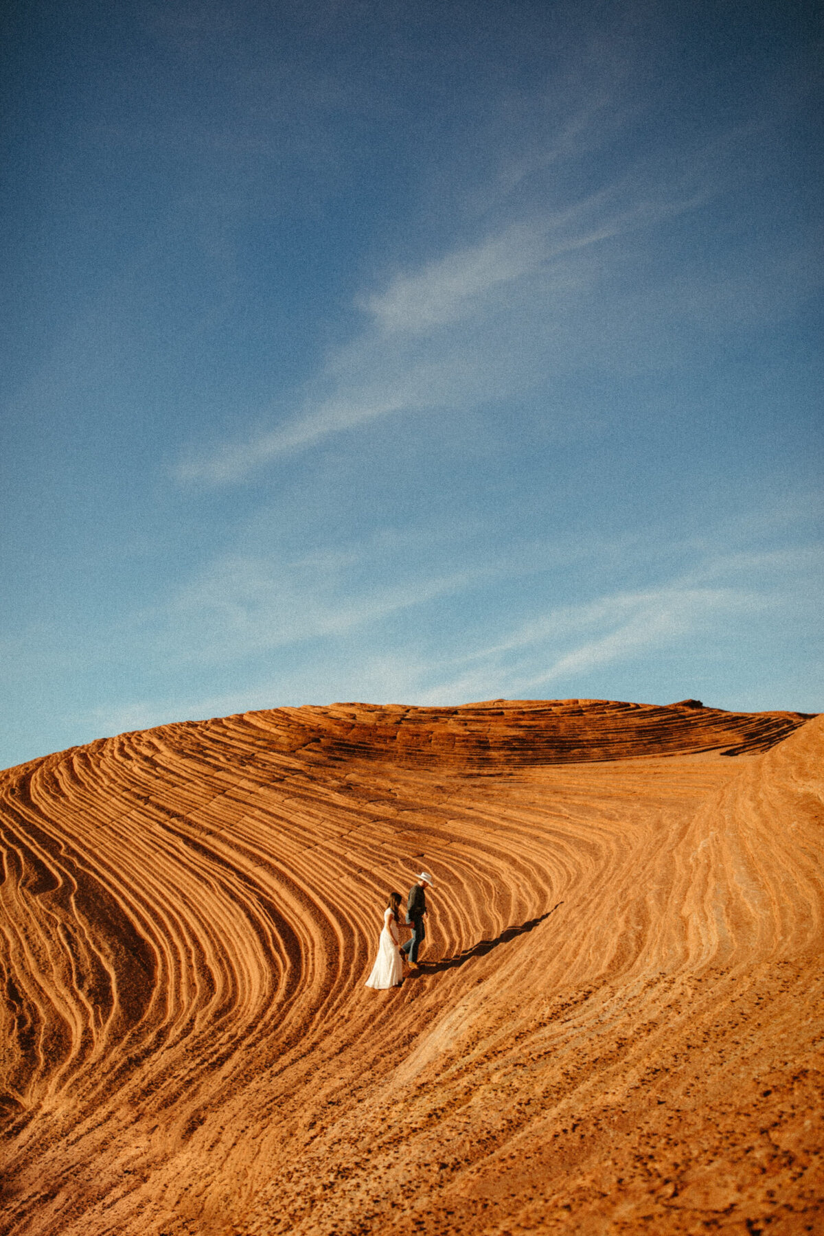 A couple is holding hands and walking along the petrified dunes in Snow Canyon State Park.