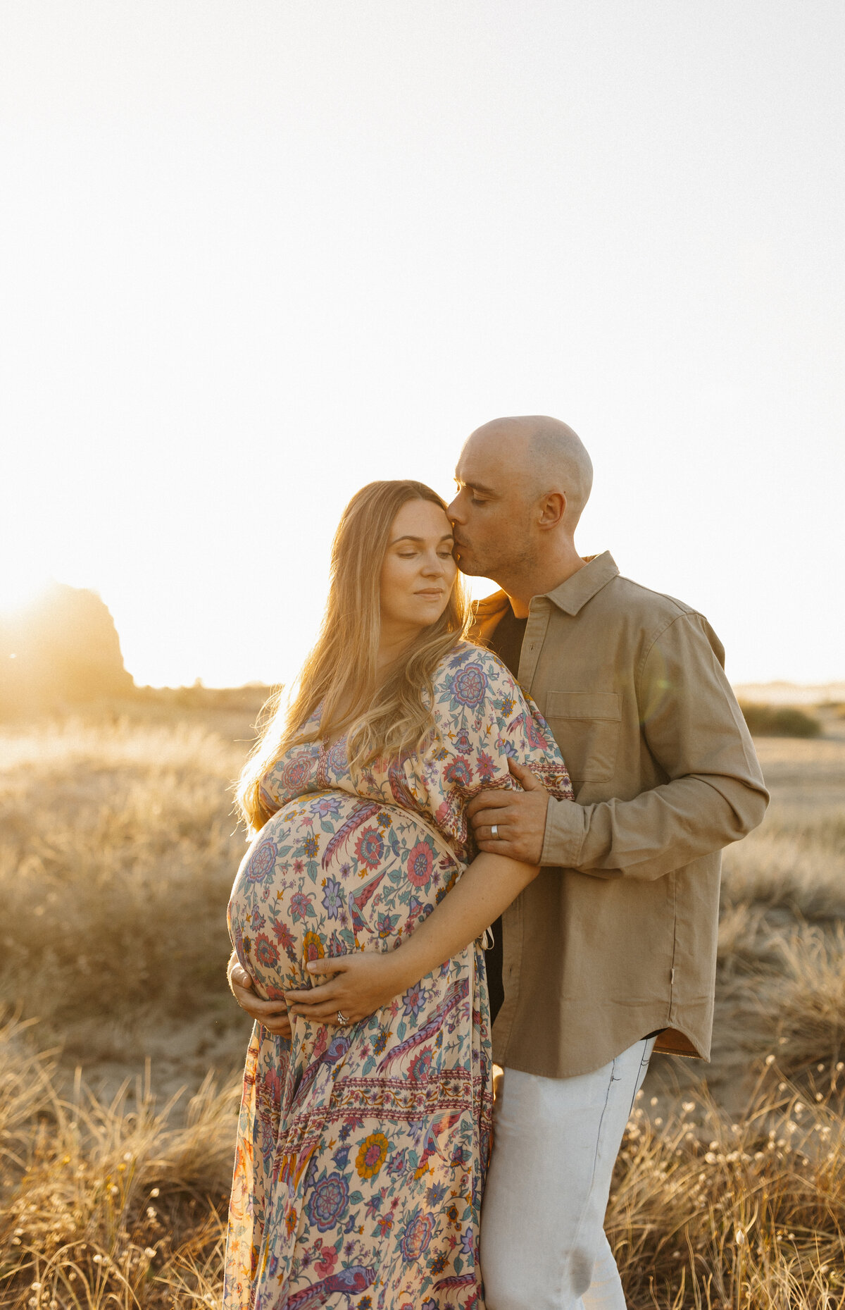 A mother and father standing with the sunset behind them during a maternity photoshoot with christchurch photographer lucy jane