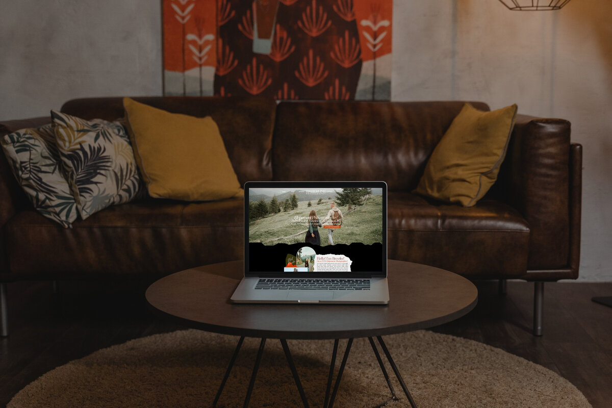 A mock up including a laptop on a cofee table with the homepage o the timberline photography website on screen with a modern leather couch in the background