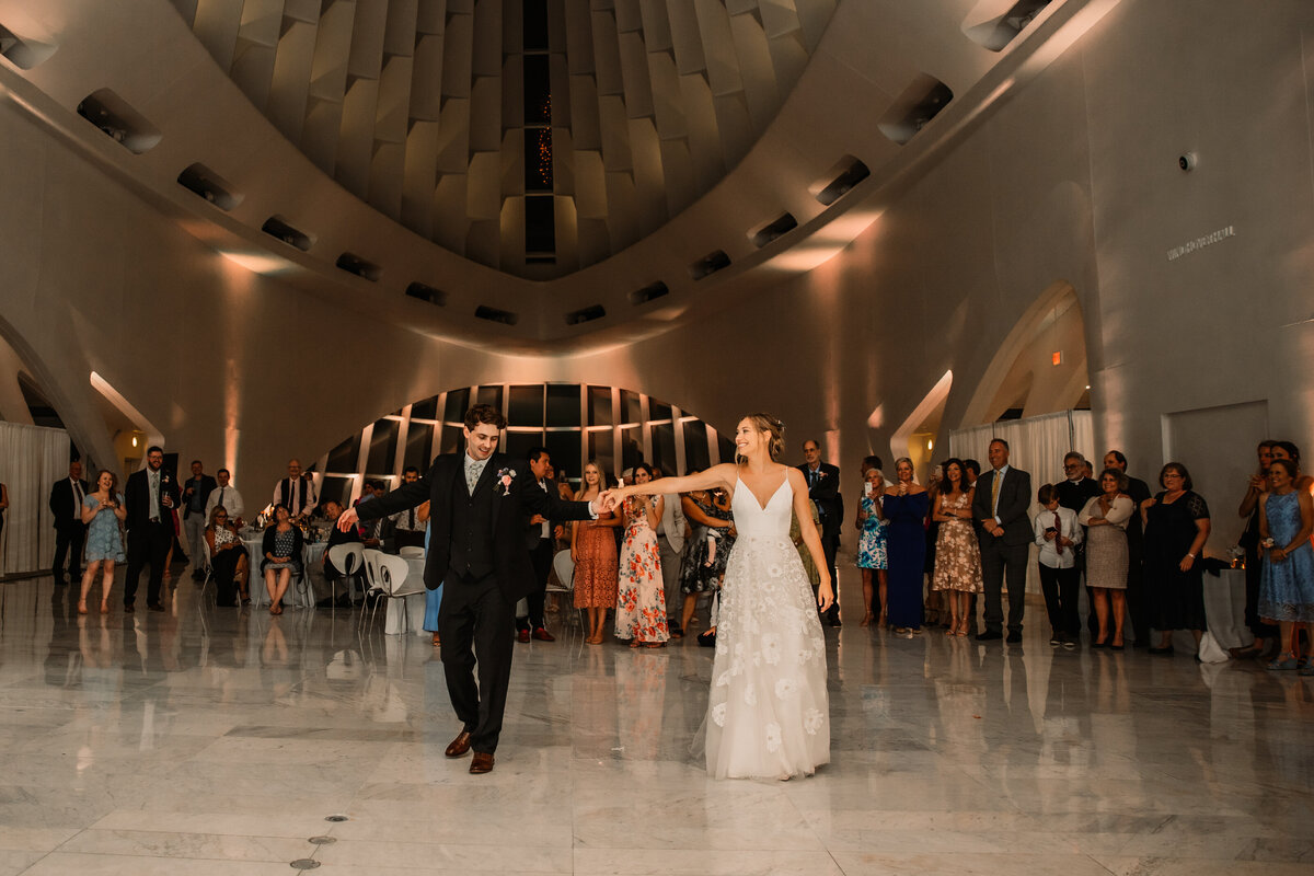 Newlyweds Dance Holding Hands as guests watch behind them