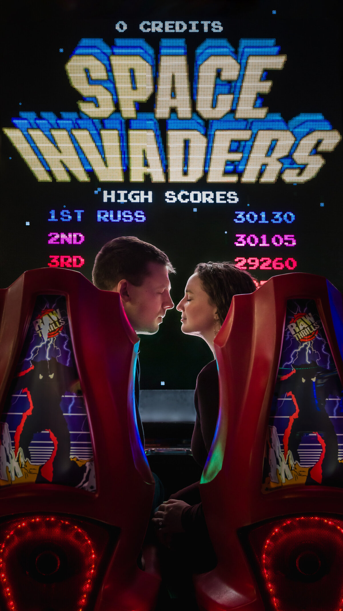 An engaged couple enjoying a fun and playful moment at an arcade during their engagement session, surrounded by vibrant lights and games, capturing their unique connection and joyful energy.
