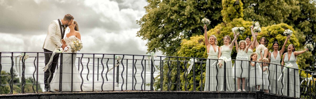 Groom and bride kissing on the bridge while guests are looking.