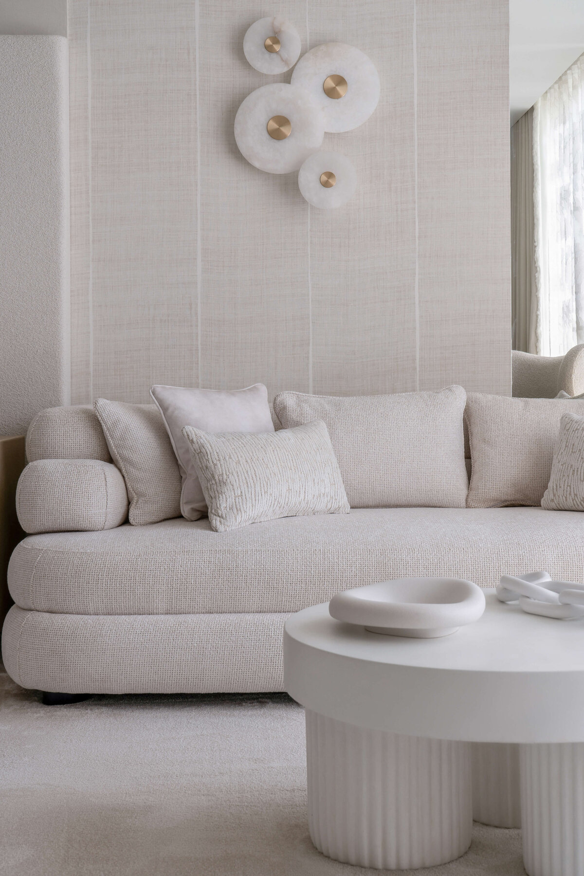 A white couch and contemporary white coffee table in the sitting area of a light, neutral primary bedroom.