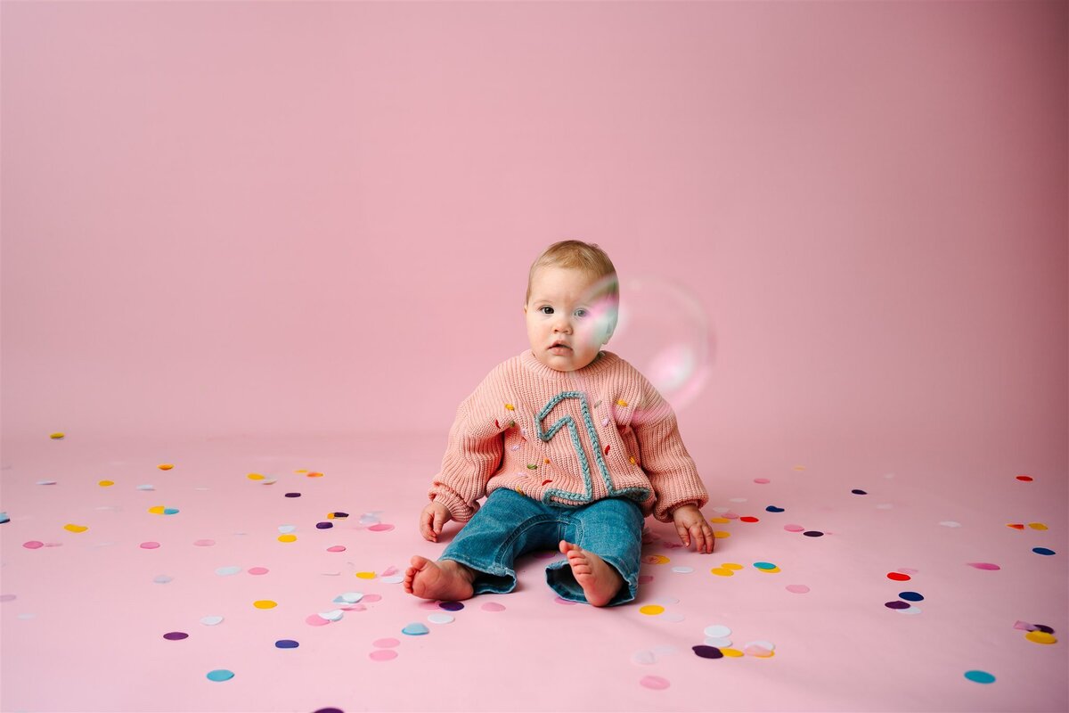 A small baby sitting down and looking at a bubble 